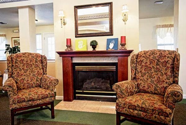 Two chairs in front of a fireplace in the community living room of Pinewood Place