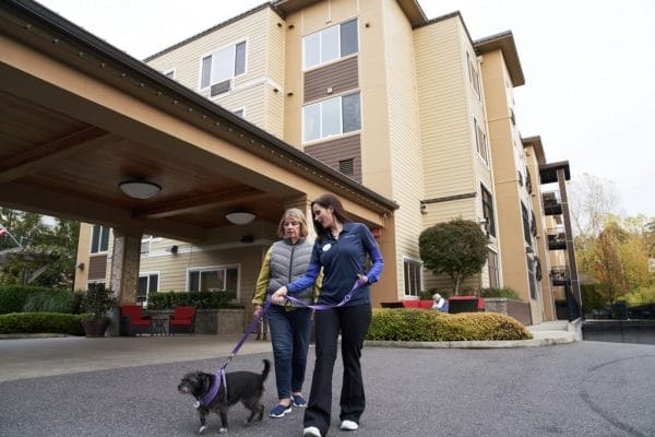 Two women walking a black dog in front of Aegis Living Bellevue