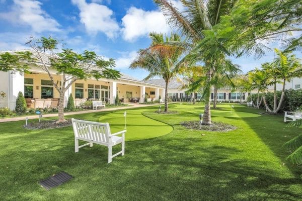Outdoor seating and a putting green under a palm tree on the grounds of Courtyard Gardens Senior Living