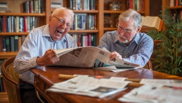 Two senior men lauging while reading the newspaper in The Terrace at Priceville