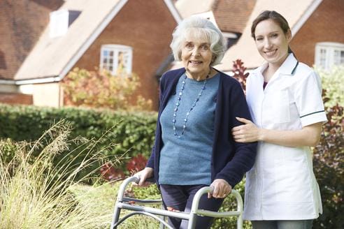 Senior woman in walker embraced by female Assisted Care Services caregiver