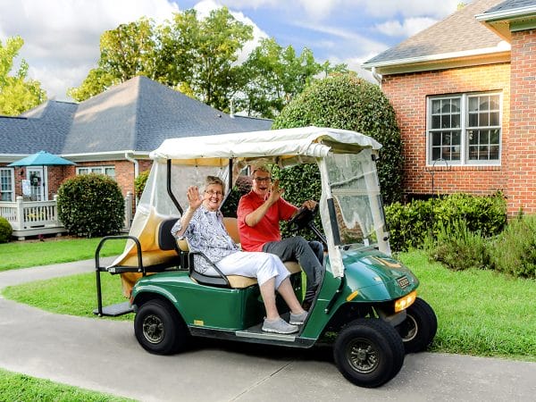 Senior couple waving from a golf cart at Martha Franks Baptist Retirement Center