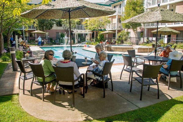 4 women sitting under an umbrella at a poolside table at Baywood Court