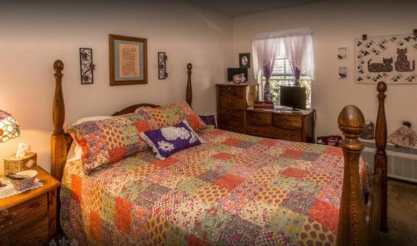 Model bedroom with patchwork quilt on bed, window with tv on dresser in front of a window at Canterbury Court