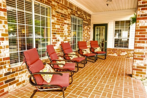 Brick paver covered front porch with red cushioned chairs on the front porch of Bridgewood Gardens