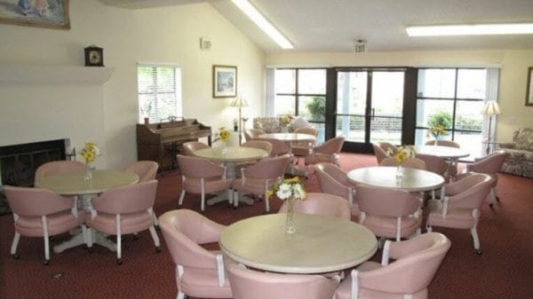 Community living area with tables, chairs and a piano at Canterbury Court