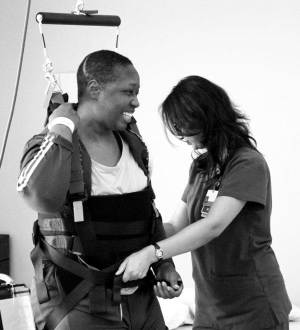 Woman in harness being assisted by an Encompass nurse