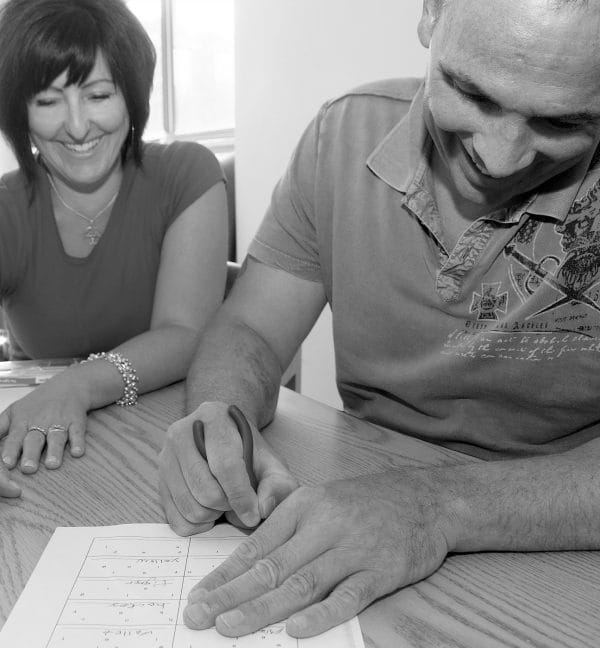 Grinning man signing paperwork with female behind him smiling