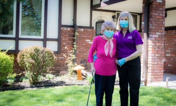Elderly woman and Home Instead staff member wearing masks and standing outside in front of residence
