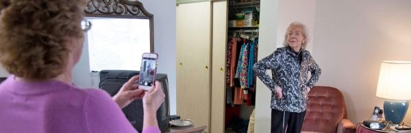 Senior woman posing in front of closet while caregiver takes photo