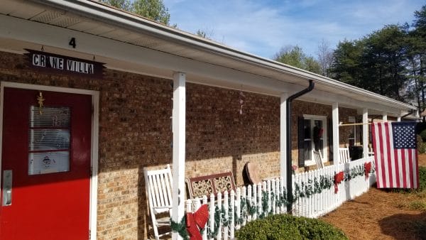 Shuler Health Care Assisted Living entrance to brick front building with rocking chairs under porch