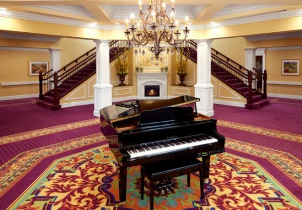 The Bristal Assisted Living Lake Grove lobby with a grand piano and a split staircase in the background