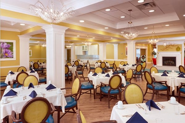 Main dining room with yellow and blue arm chairs and white pillars and coffered ceiling at The Bristal Assisted Living at Englewood
