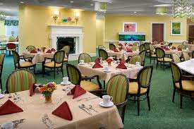 The Bristal Assisted Living at Holtsville dining room with yellow walls and green and gold arm chairs with large white fireplace