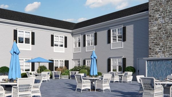 The Bristal Assisted Living at Somerset outdoor patio with white tables with blue umbrellas and the main building with black shutters in the background