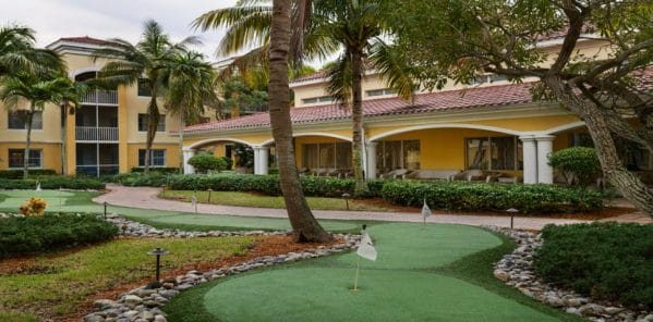 Putting green and palm trees with covered porches in the background at The Carlisle Naples
