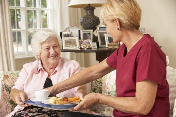 Female caregiver serving senior woman food from a tray