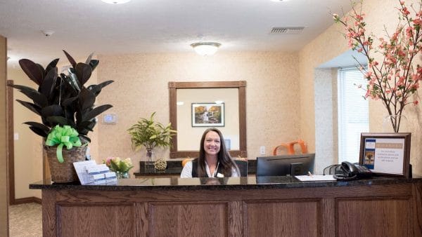 Smiling woman at front desk greeting residents at Ashwood Square Retirement