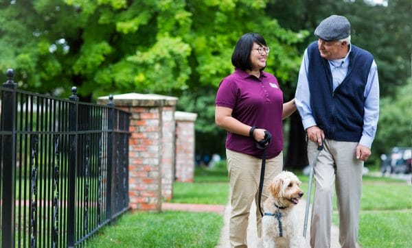 Woman in purple shirt walking a dog with senior man