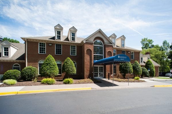 Front entrance with brick building fascade and blue awning at Commonwealth Senior Living at Georgian Manor