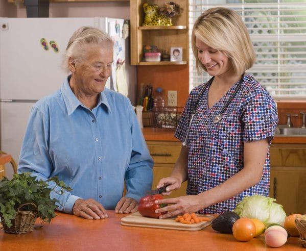 Americare Plus caregiver cutting vegetables in the kitchen with senior man