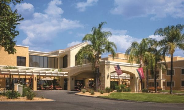 Main entrance with covered driveway and palm trees at Gladwell at Atria Senior Living