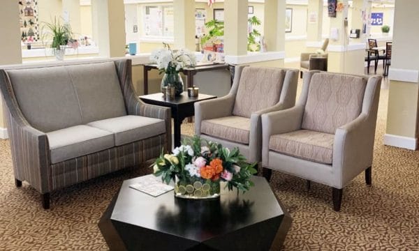 Sitting area with a loveseat, two chairs and a coffee table with flowers at Lassen House Senior Living