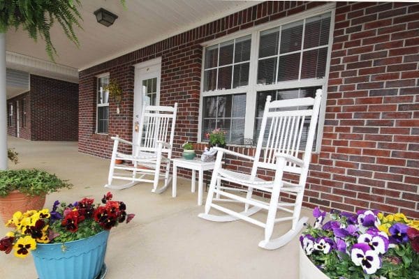 White rocking chairs surrounded by flowers on the porch of The Madison Village