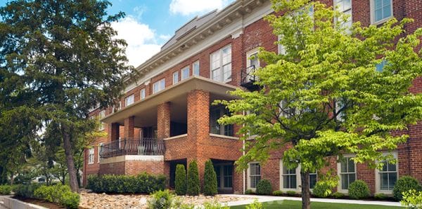 Exterior of the brick fascade at Oak Wood Place Senior Living with large covered balcony and green trees