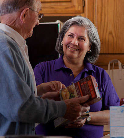 Female caregiver helping senior man in kitchen