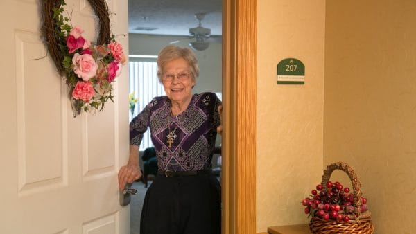 Senior woman smiling at her apartment door with wreath at Robinwood Retirement