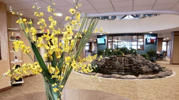 Close up of yellow flower arraingement with indoor water fountain in the lobby of Sable Lodge Retirement