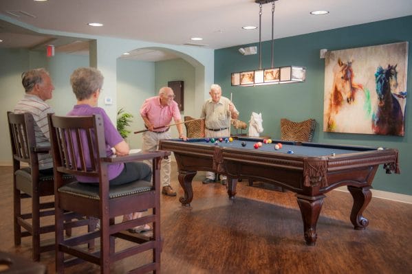 Seagrass Village of Fleming Island residents playing pool in the billiards room while seniors in chairs watch