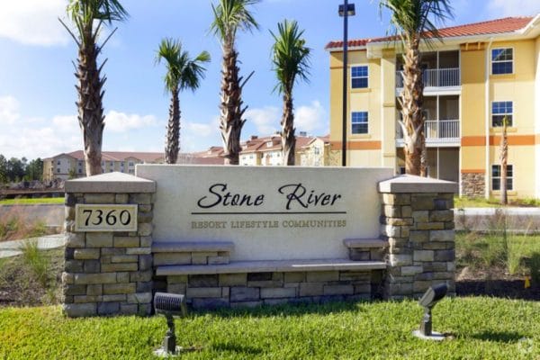 Stone River Retirement front entrance with stone work sign and building and palm trees in the background