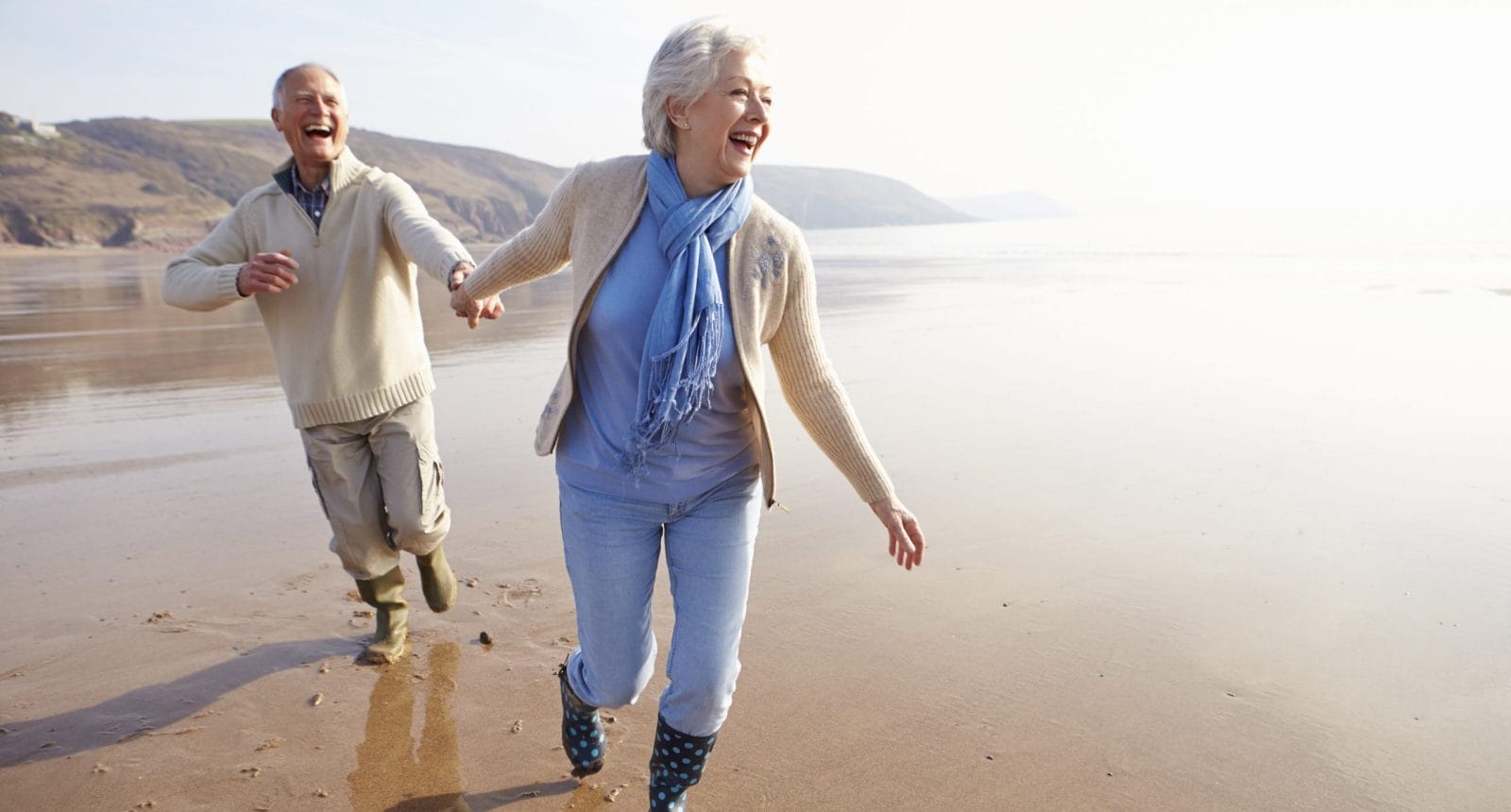 Senior man and woman holding hands and jogging on the beach