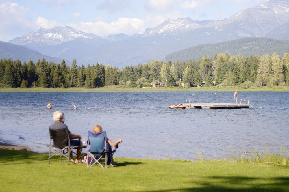 Senior couple sitting in chairs facing a lake with mountains in the background