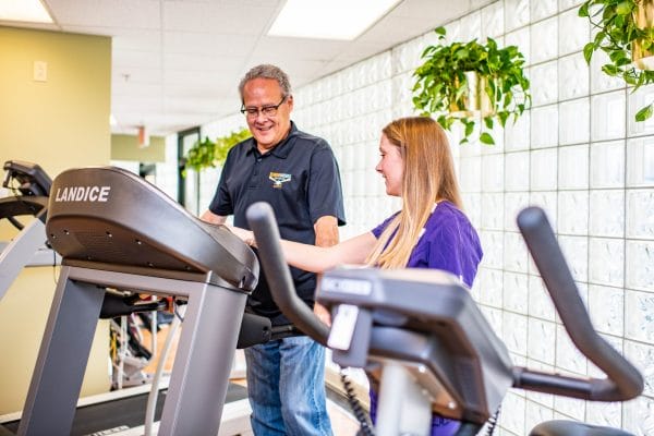 Female therapist helping senior man with treadmill