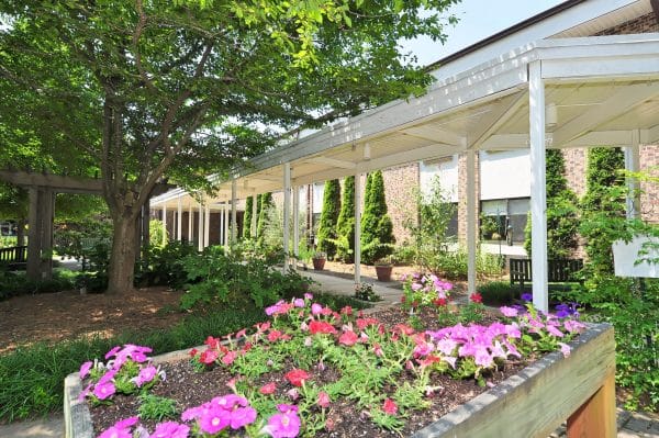 Covered outdoor walkway surrounded by flowers on the grounds of Western North Carolina Retirement Home