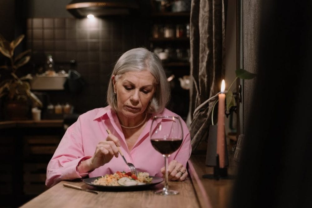 Senior woman in a pink shirt eating a meal with a glass of wine