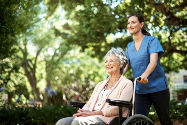 Senior woman in wheelchair being pushed by Compassionate Care caregiver