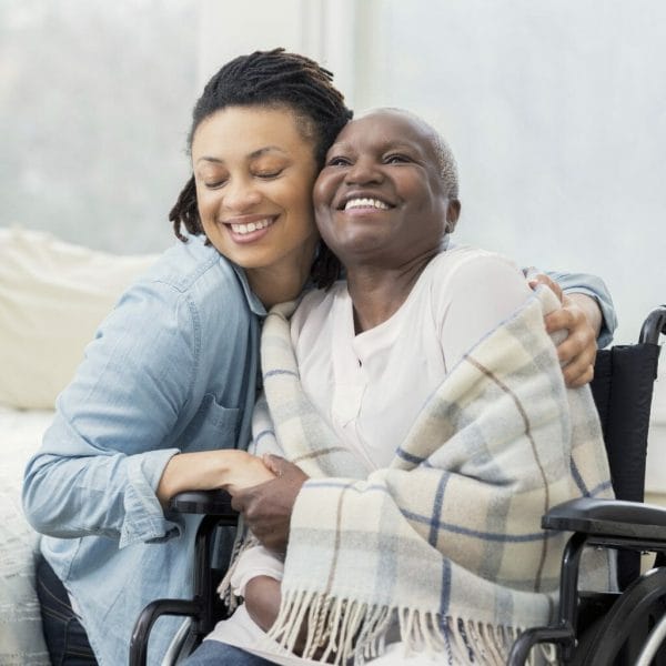 Compassionate Care caregiver embracing senior woman in wheelchair