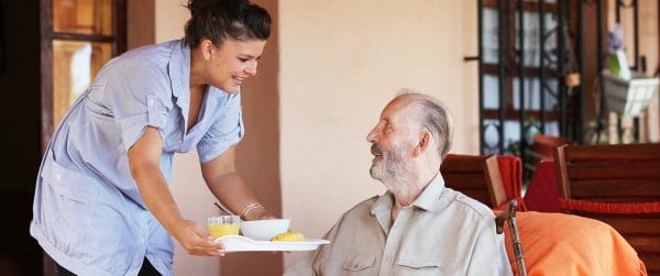 Senior man smiling as a Around the Clock Home Care caregiver brings him a tray of food