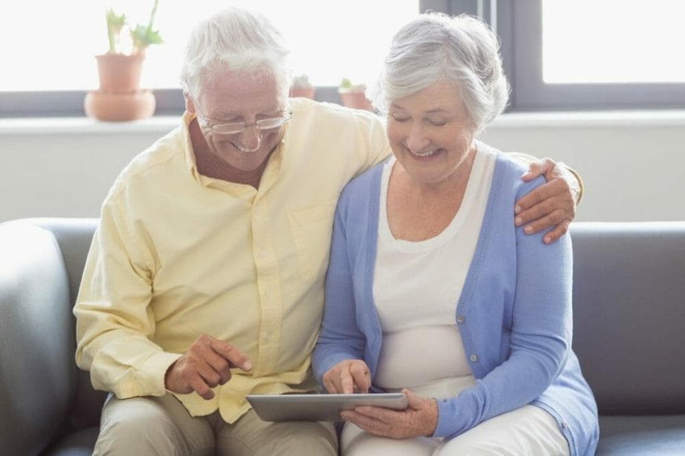 Senior couple sitting down looking at a tablet computer and smiling