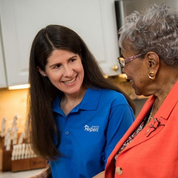 Senior Helperscaregiver with long black hair and a blue shirt smiling with a senior woman