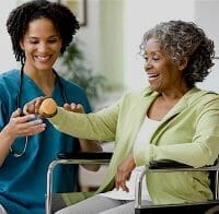 Excellence Home Healthcare Care Giver doing therapy with elderly lady in green sweater in wheel chair