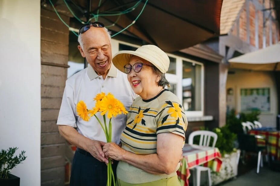 Senior couple aem in arm while holding sunflowers and smiling