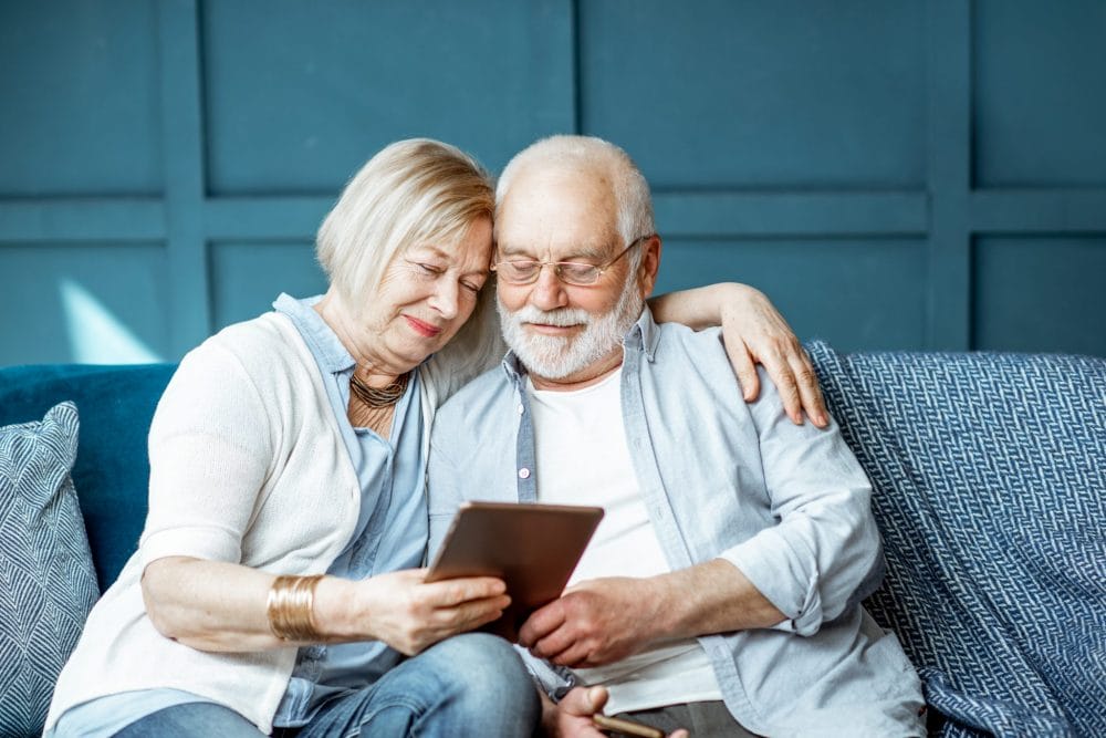 Senior couple embracing on a sofa and looking at a tablet